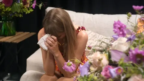 Disney Taylor Swift holds a tissue to her face as she cries in a dressing room filled with bouquets of flowers